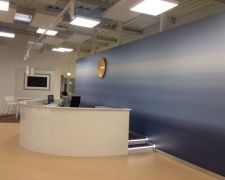 Halbrunder, weiß glänzender Empfangstresen vor einer beidseitigen Akustikwand